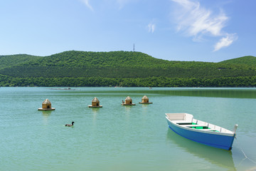 Fototapeta na wymiar Bright blue empty rowing boat and duck houses on the green water of the mountain lake Abrau-Durso