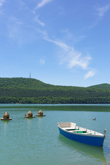 Fototapeta na wymiar Bright blue empty rowing boat for riding on the green water of the mountain lake Abrau-Durso