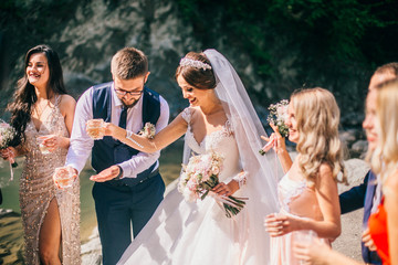 Wedding day bride and groom with bridesmaids and groomsmen posing in sunlight evening in mountains near river gorgeous wedding newlyweds couple with best friends.  People drink champagne and hugging. - obrazy, fototapety, plakaty