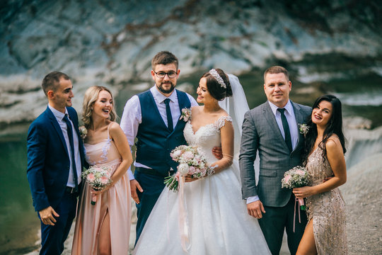Wedding day bride and groom with bridesmaids and groomsmen posing in sunlight evening in mountains near river gorgeous wedding newlyweds couple with best friends.  People drink champagne and hugging.