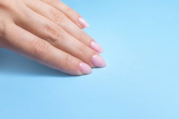 Women's hands with perfect Nude manicure. Nail Polish is a natural pale pink shade. Blue background