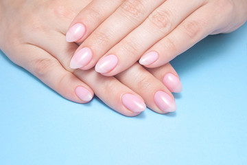 Women's hands with perfect Nude manicure. Nail Polish is a natural pale pink shade. Blue background