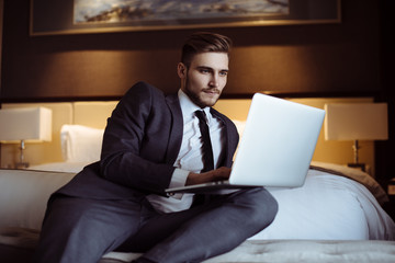 Young handsome businessman talks on-line with his business partners at the hotel room. Hotel service. Booking hotel. Freelancer sitting on his sofa in a hotel room and working with his computer. 