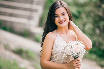 Portrait of a beautiful bridesmaid posing with bride's wedding bouquet in city streets with green...