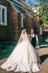 Obraz premium Bride and groom holding hands and walks near brick wall at wedding day. Newlyweds after wedding ceremony.
