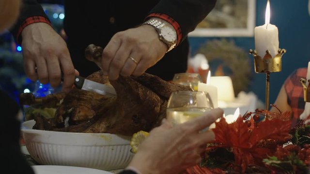 Father of family with children and parents at table carving roasted turkey while celebrating Christmas holiday at home