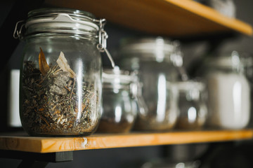 Glass transparent jar with green tea stands on a wooden shelf.