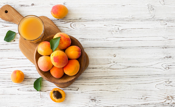 Ripe apricots and glass of juice in wooden bowl