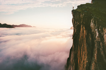 Traveler standing on cliff edge mountain top above sunset clouds travel adventure lifestyle summer...