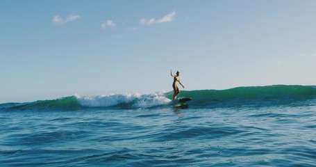 Beautiful young Hawaiian woman surfing at sunset