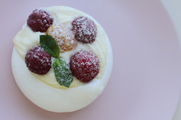 White meringue cake with yellow and red raspberries on pink plate, place for text