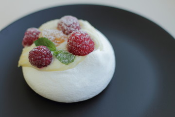 white meringue cake with yellow and red raspberries on black plate, place for text 