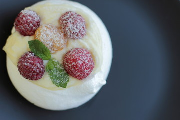 white meringue cake with yellow and red raspberries on black plate, place for text 