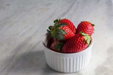 Heap fresh strawberries in the white porcelain bowl on the grey table background