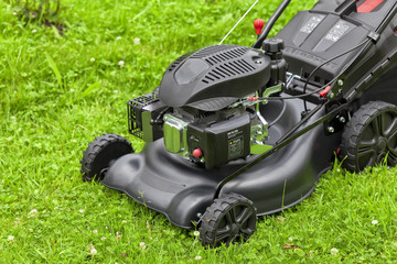 Fototapeta premium A four-stroke gasoline lawnmower on top of the grass in the garden
