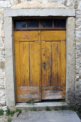 Fototapeta na wymiar Old yellow wooden doors with small glass top windows and heavy stone frame put in traditional stone wall