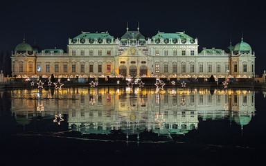 Fototapeta na wymiar Upper Belvedere Palace with Christmas Village reflecting in the pond covered with wet ice in night, Vienna, Austria