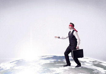 Young blindfolded businessman steps on a realistic globe