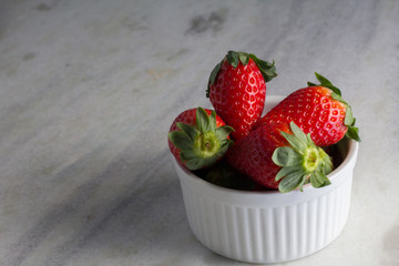Heap fresh strawberries in the white porcelain bowl on the grey table background