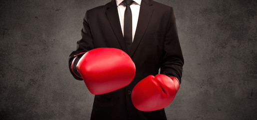 A well dressed sales person standing with red boxing gloves on his hand in front of urban grey wall background concept.