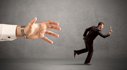Young miniature businessman running from a big hand with light grey background