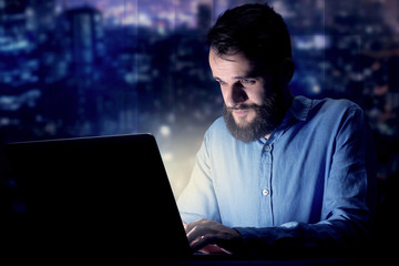 Young handsome businessman working late at night in the office with blue lights in the background