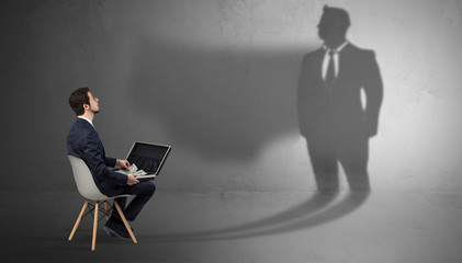 Humble businessman staying and offering stuffs to a huge businessman shadow

