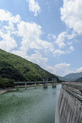 Side view of a dam with a mountain forest & clouds