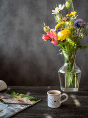 Bouquet of flowers in vase, cup of coffee and magazine on wooden rustic table.
