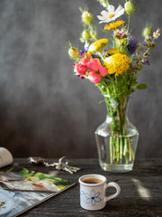 Bouquet of flowers in vase, cup of coffee, magazine and bunch of keys on wooden rustic table.