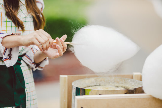 Theme is a family small business cooking sweets. Hands close-up Young woman trader owner of the outlet makes a candy floss, fairy floss or Cotton candy in the park in summer