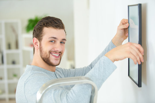 happy man positioning picture frame on wall