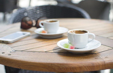 two cups of espresso on a table with marmalade and sunglasses and a phone in the background