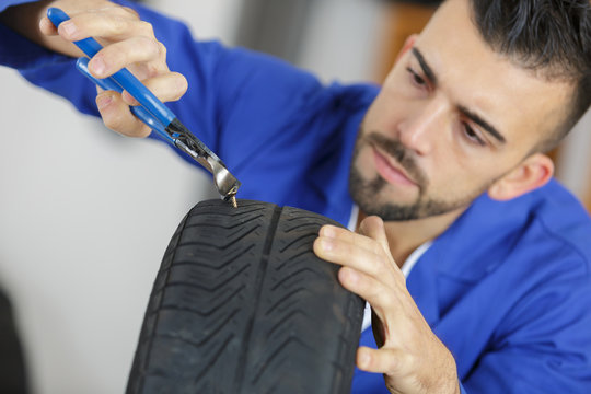 auto mechanic taking nail out of tire with claw