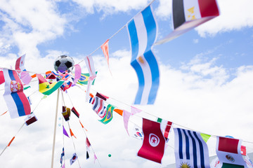 Different country flags weaving on a rope with a soccer ball in the center. Photo of a various country flags weaving on wind and blue sky on a background.