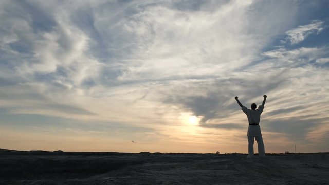 Athlete triumphantly raises his hands up at sunset