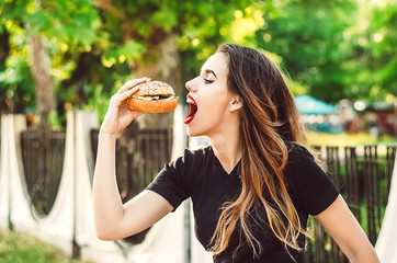 a girl with one hand wants to bite a hamburger with a stuffing. food and people