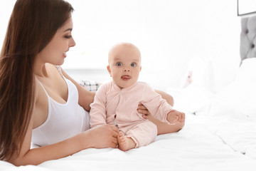 Young mother with her cute baby girl on bed at home