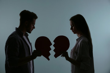 Silhouette of couple with torn paper heart on color background. Relationship problems