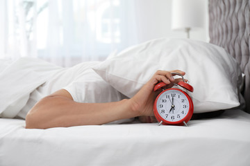 Man turning off alarm clock in bedroom - obrazy, fototapety, plakaty