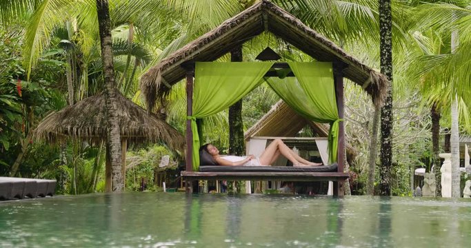A beautiful woman in a luxury resort, relaxes on loungers by the pool and while swimming. Concept of: travel, vacation, relaxation, hotel.