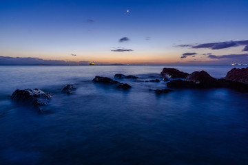 Obraz premium 夜明けの三日月と金星が輝く磯で