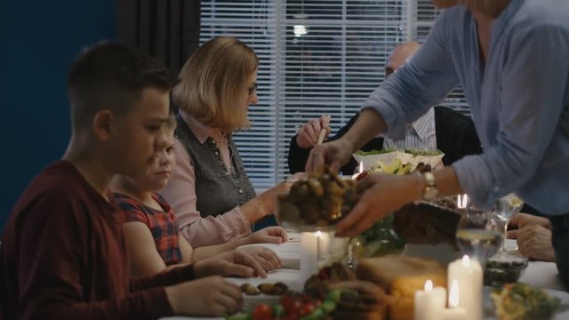 Happy family with grandparents and children sitting at table with abundance of feast food celebrating Thanksgiving day and communicating