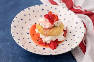 Homemade Strawberry Shortcake in White Bowl with Blue Stars; Red and White Striped Towel; Blue Background