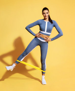 Woman with good physique doing stretching work out with elastic bands. Photo of latin woman in fashionable sportswear on yellow background. Strength and motivation.