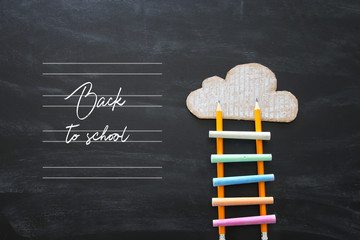 ladder made of colorful chalks and pencils next to clouds over blackboard background.