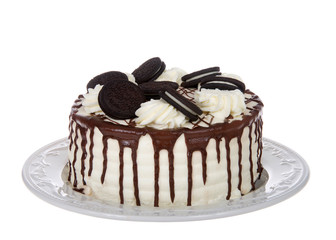 White whipped cream frosted cake with chocolate cream filled sandwich wafer cookies, melted chocolate melting down the sides on a porcelain plate, isolated on white background.