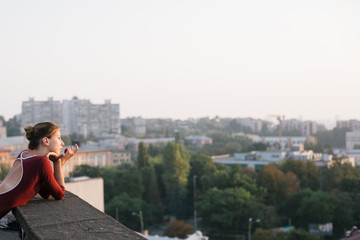 Young and graceful ballerina contemplating sunset cityscape from the roof of city building