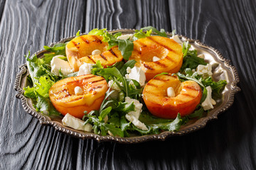 Fresh summer salad with grilled peaches, with feta cheese, peanuts and greens close-up on a plate on a table. horizontal