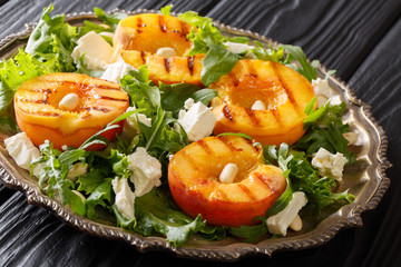 Salad with organic grilled peaches, with feta cheese, peanuts and herbs closeup on a plate on the table. horizontal